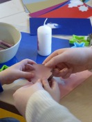 Kinder und Erzieherinnen verzieren Kerzen mit bunten Wachsplatten.